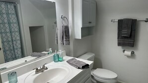Un bany amb un lavabo blanc, un mirall, un vàter i una barra per a tovalloles.