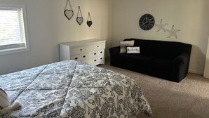 Una camera da letto con un letto, una cassettiera bianca, un divano nero e decorazioni a parete.