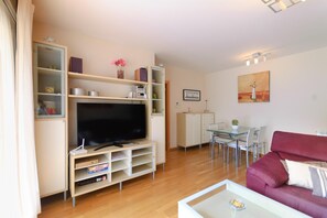 Ein modernes Wohnzimmer mit Flachbildfernseher, Holzboden, einem roten Sofa und einem Glastisch.