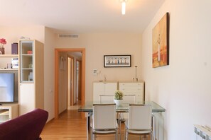 Ein modernes Wohnzimmer mit einem Glastisch, weißen Stühlen, einem roten Sofa, einem Bücherregal und einem Gemälde an der Wand.