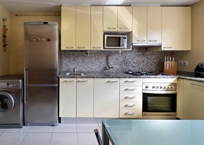 Eine kompakte Küche mit Edelstahl-Kühlschrank, Mikrowelle, Herd und Waschmaschine.
