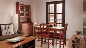 A cozy dining area with a wooden table and chairs, a cabinet with glass doors, and a large window with a view of buildings.