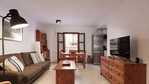 A living room with a sofa, a wooden coffee table, a TV, and a dining area with a table and chairs.
