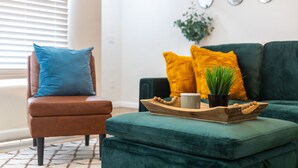 A living room with a brown leather chair, a green sofa, and a wooden tray with a plant and a mug. - The Yuma White Modern Pool/Pet friendly Home (Yuma)