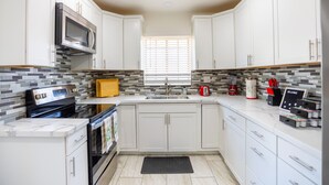 A modern kitchen with white cabinets, a stainless steel microwave, a built-in oven, and a tiled backsplash. - The Yuma White Modern Pool/Pet friendly Home (Yuma)