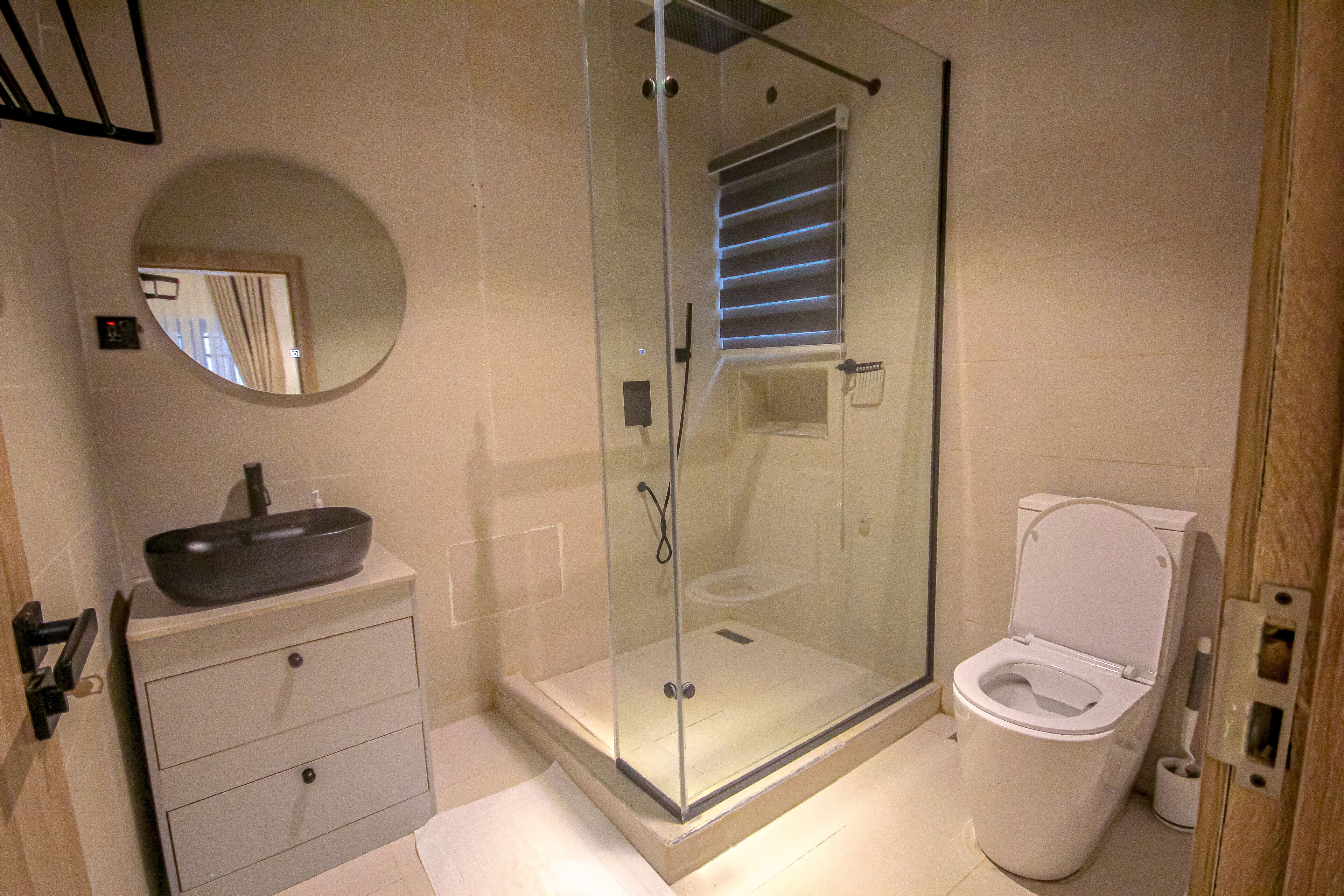 A bathroom with a glass-enclosed shower, a vessel sink, a toilet, and a mirror.