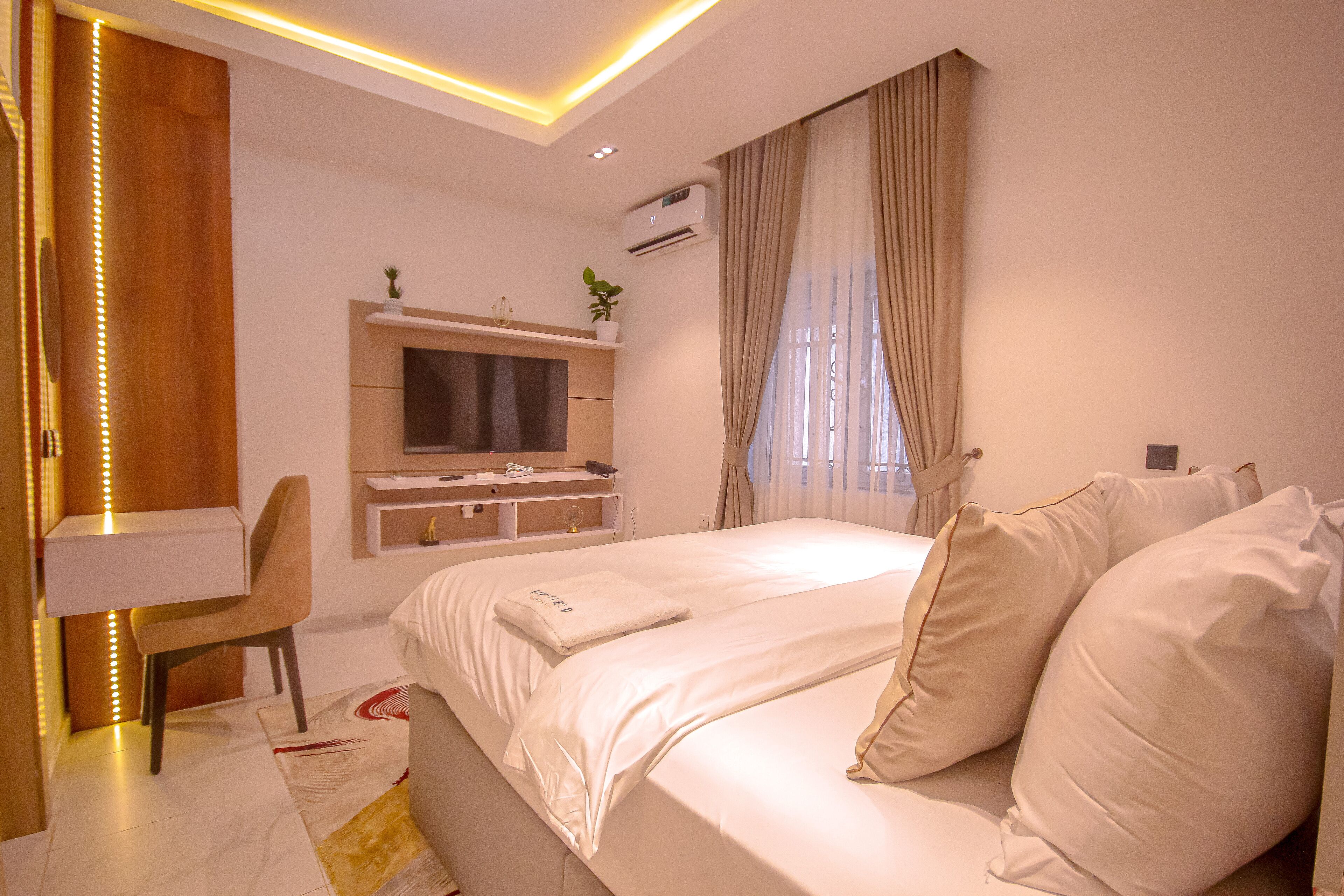 Ein modernes Hotelzimmer mit einem großen Bett, einem Schreibtisch, einem Fernseher und einer Klimaanlage.