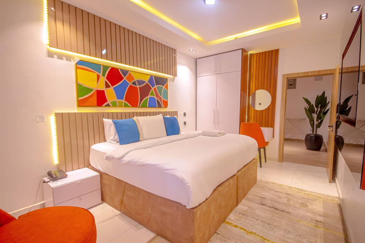 Une chambre moderne avec un grand lit, des tables de chevet, un tableau abstrait aux couleurs vives et un miroir.