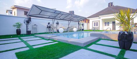 Patio trasero con piscina, un porche cubierto y una casa al fondo.