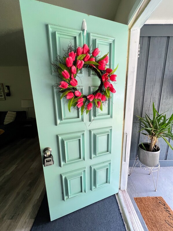 A teal door with a wreath of pink flowers and a potted plant beside it.