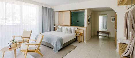 A modern hotel room with a bed, two chairs, a small table, a mirror, and a walk-in closet.