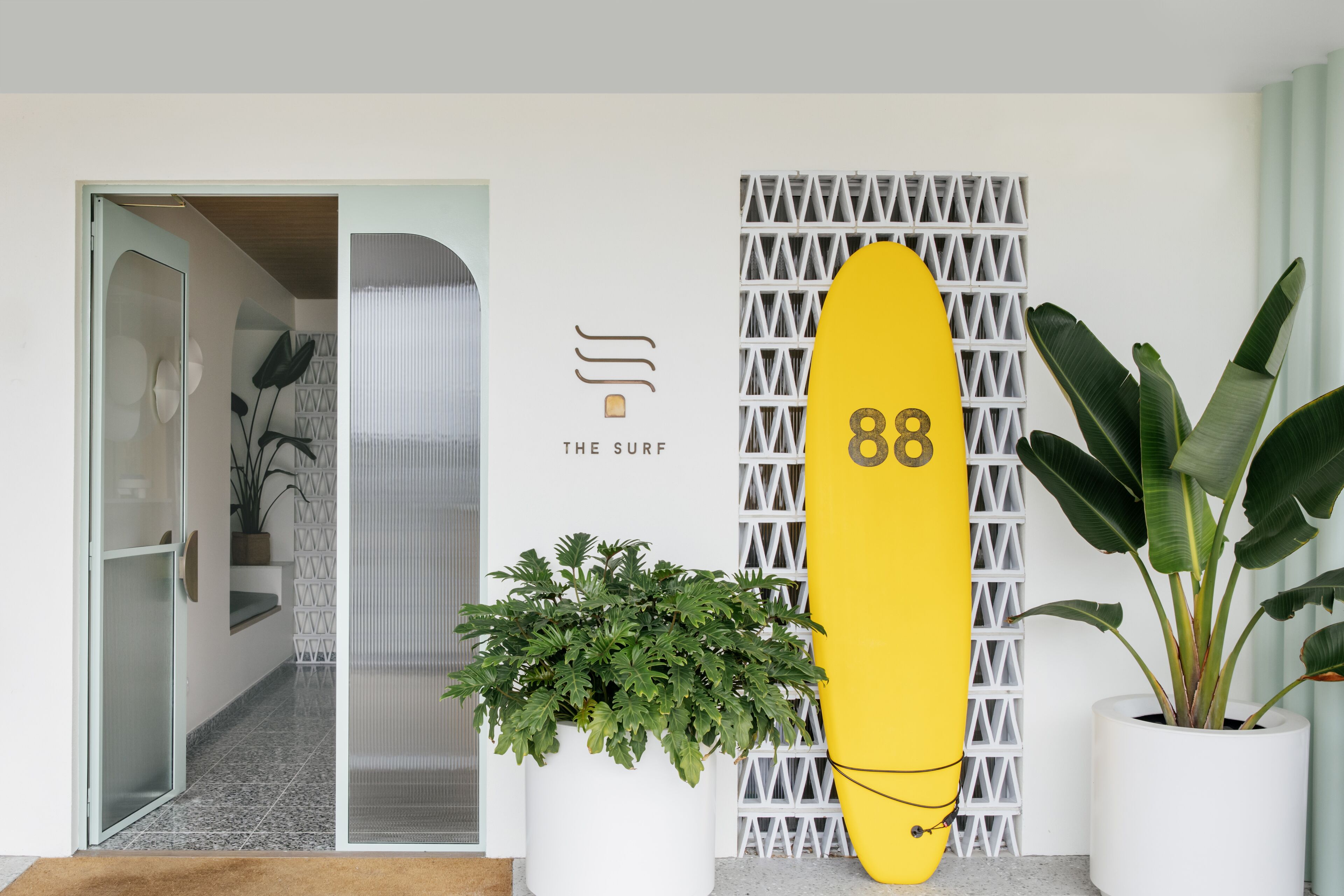 Un interior moderno con un símbolo de número con forma de tabla de surf, una planta en maceta y un diseño geométrico en la pared.