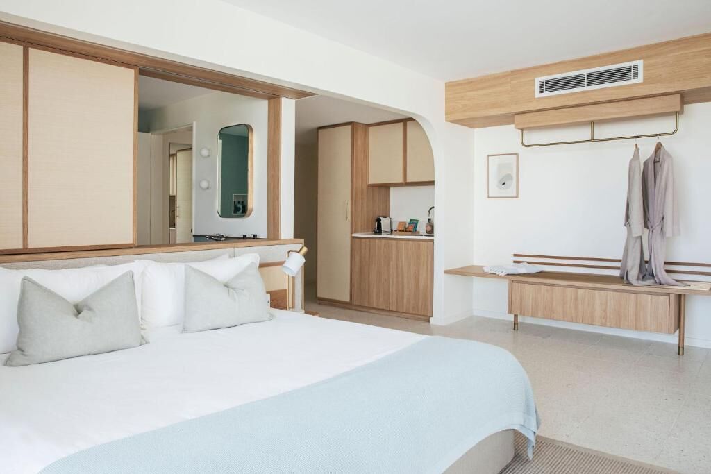 Quarto de hotel com cama grande, guarda-roupa, penteadeira com espelho e um banco.