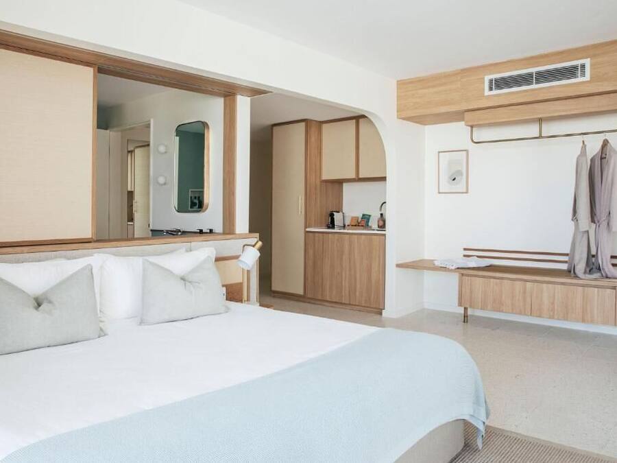 Quarto de hotel com cama grande, guarda-roupa, penteadeira com espelho e um banco.