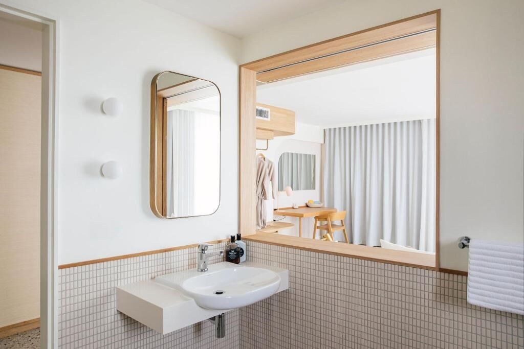 Un baño moderno con un lavabo blanco, un espejo grande y suelo de baldosas.