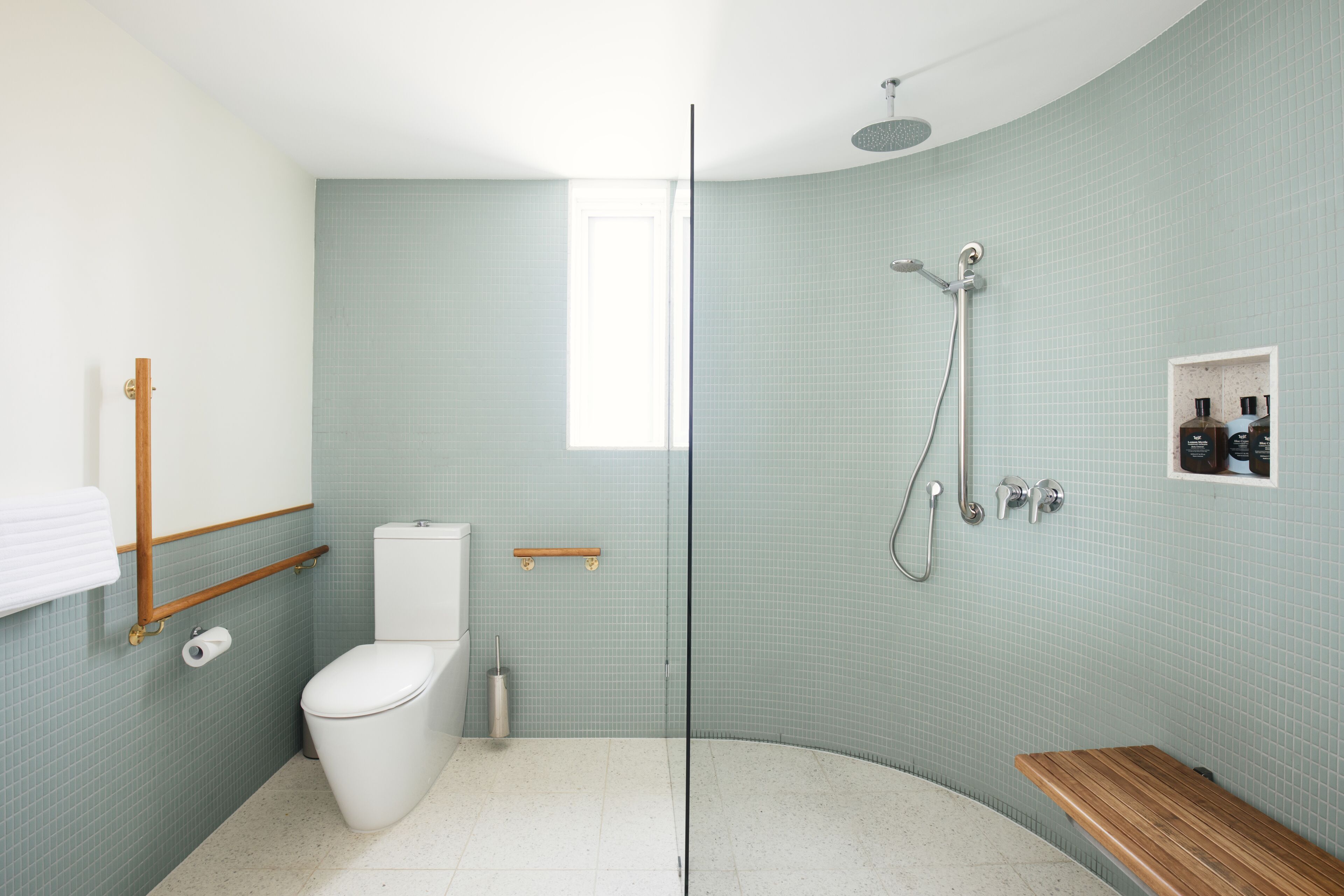 A modern bathroom with a glass shower enclosure, a toilet, and a wooden bench.