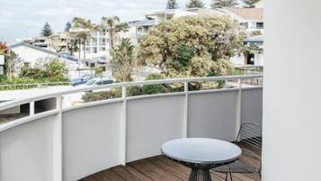 A balcony with a wooden floor, a round table, and two wire chairs.