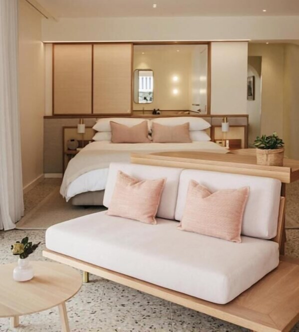 Un dormitorio moderno con una cama grande, un sofá, una mesita y una planta en maceta.