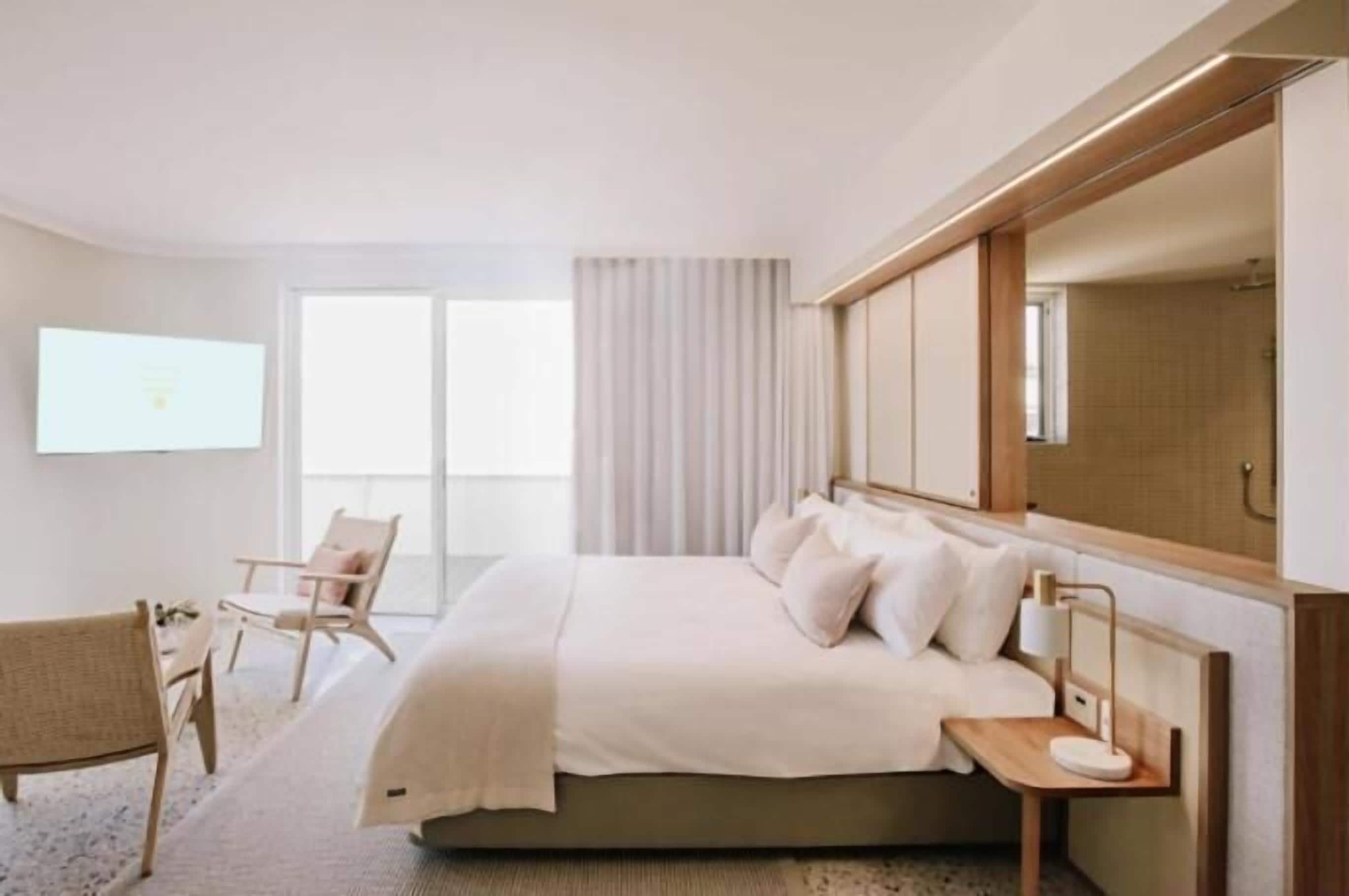 A modern hotel room with a large bed, a desk, a chair, and a TV.