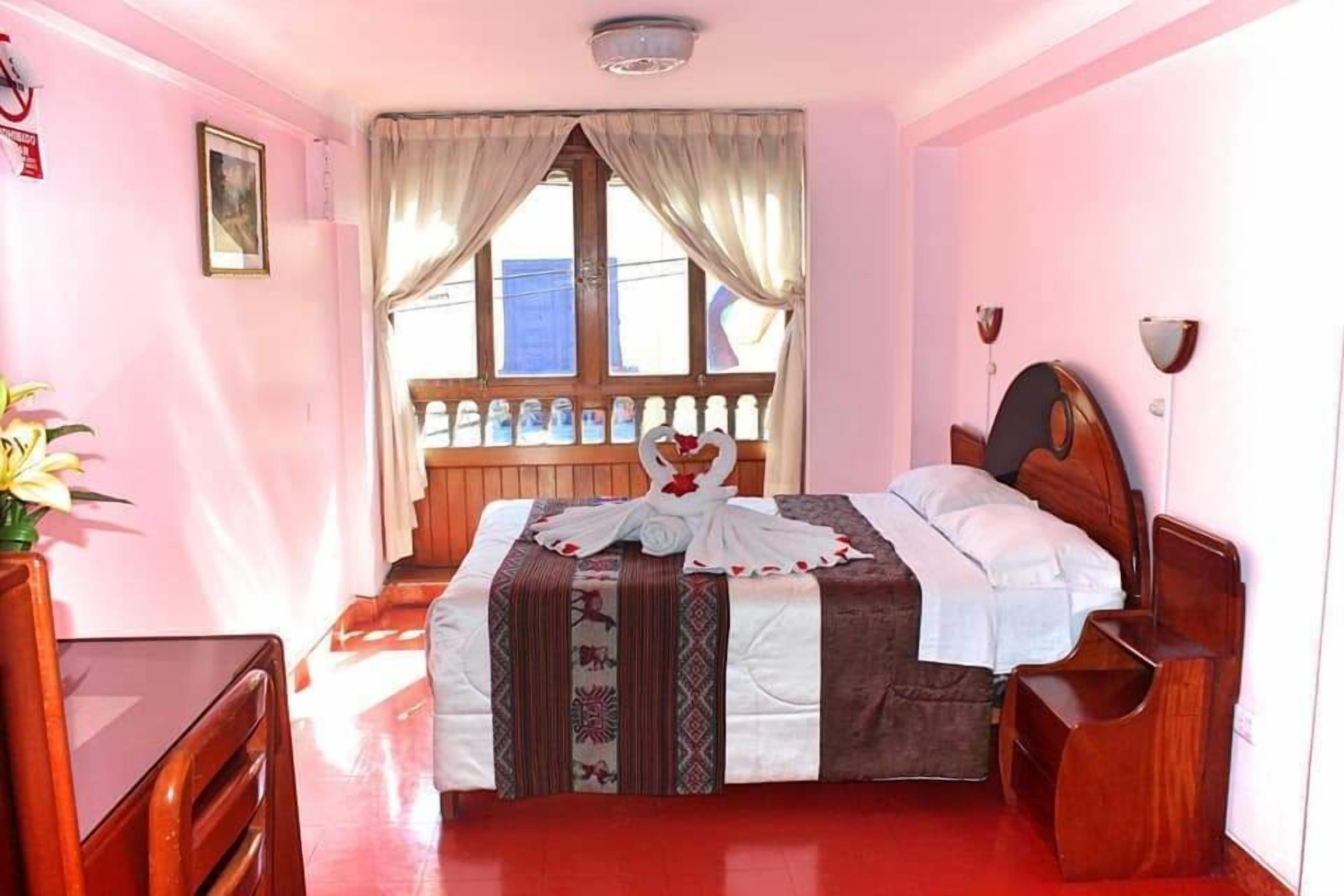 A bedroom with a bed, wooden furniture, a window with curtains, and a vase with flowers.