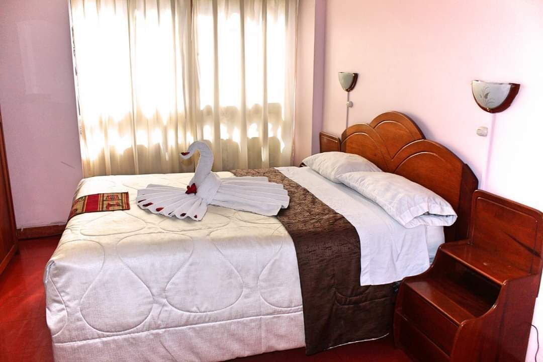 A hotel room with a bed, a wooden headboard, a bedside table, and a window with curtains.