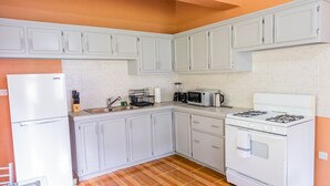 Una cocina compacta con armarios blancos, un refrigerador blanco, una estufa y un microondas.