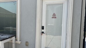 A door with a glass panel and an Airbnb logo, a window with blinds, and a small table.