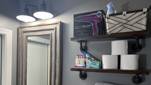 A bathroom with a large mirror, shelves with toiletries, and a towel rack.