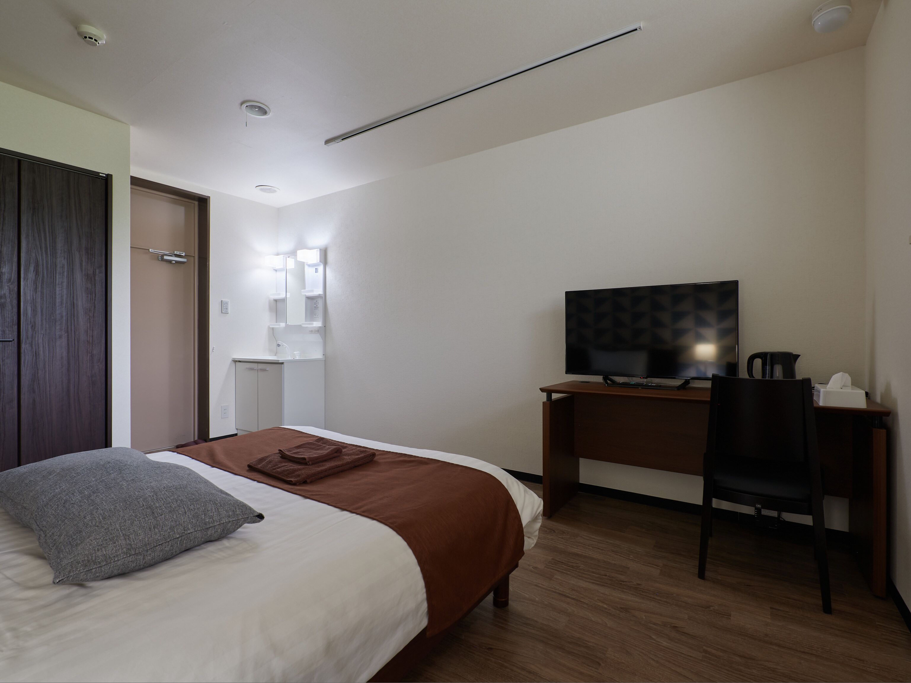 Ein Hotelzimmer mit einem Bett, einem Schreibtisch mit Computer, einem Sessel, einem Fernseher und einer kleinen Küchenzeile.