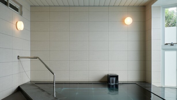 Una piscina interior moderna amb sòl i parets de rajola, una barana metàl·lica i dues làmpades murals.