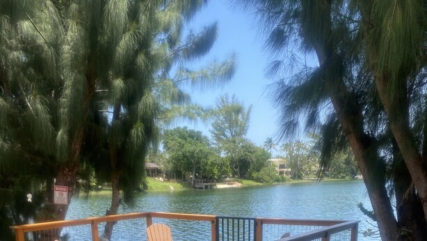 A wooden deck with chairs and a table overlooking a lake, surrounded by trees and a warning sign.