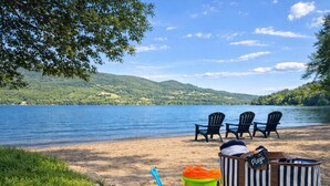 A lakeside beach with chairs, a striped bag, and beach toys. - ❤️ Mountain View and Lake Access - Mont-Tremblant (Mont-Tremblant)
