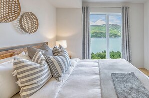A bedroom with a large bed, a view of a lake, and a window with curtains.