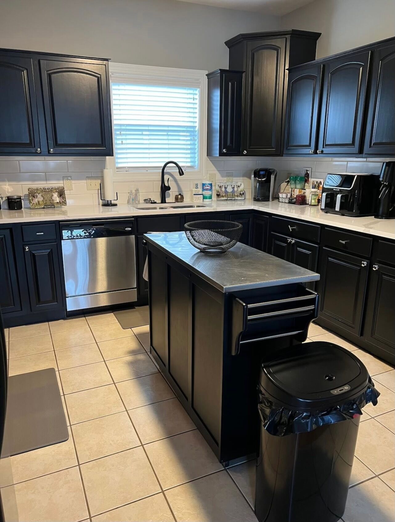 A modern kitchen with dark cabinetry, a stainless steel dishwasher, a coffee maker, and a trash can.