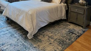 A bedroom with a large bed, two bedside tables, a chandelier, a painting, and a window with curtains.