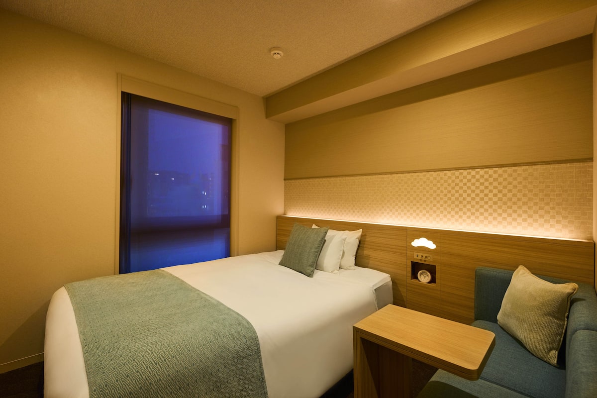 A hotel room with a bed, a small table, a sofa, and a nightstand.