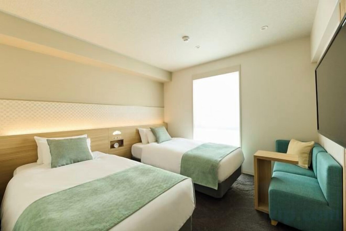 A hotel room with two beds, a sofa, a TV, and a window.