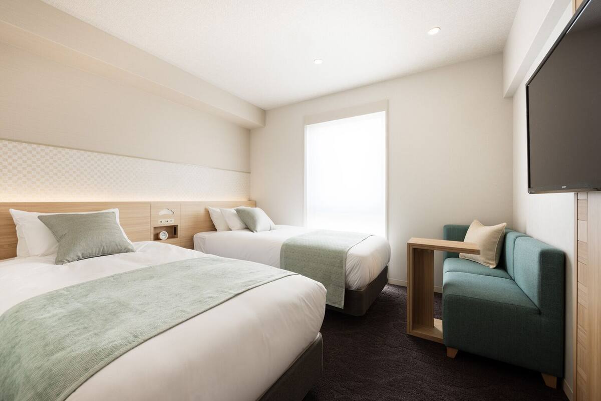 A hotel room with two beds, a TV, a small table, and a sofa.