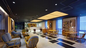 Un moderno vestíbulo de hotel con piso a cuadros, área de descanso con sillas y sofás, mostrador de recepción de madera y grandes ventanales.