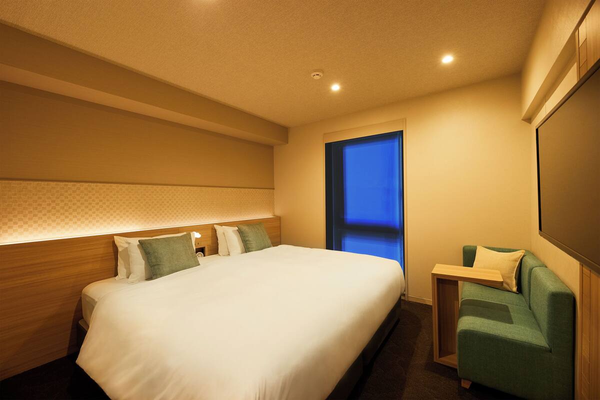 A hotel room with a large bed, a small desk, and a green armchair.