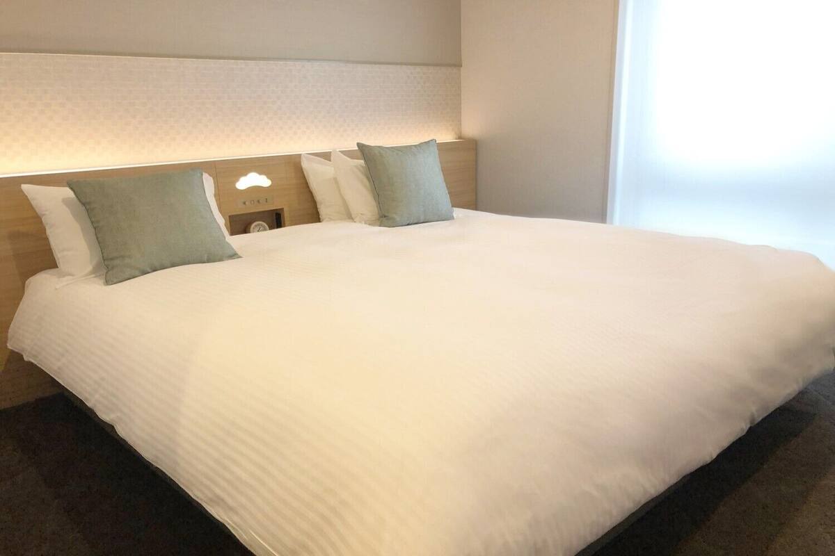 A neatly made bed with a headboard, two pillows, and a bedside table with a lamp.