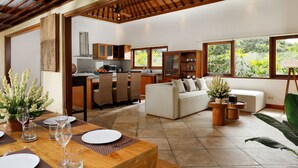 A spacious living area with a dining table set for four, a sofa, and a kitchen in the background. - Villa Perere9 by Nakula (Canggu)