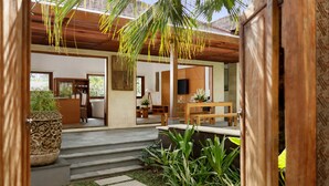 A modern house with a wooden exterior, a stone pathway leading to a wooden deck, and a view of the interior through an open door. - Villa Perere9 by Nakula (Canggu)