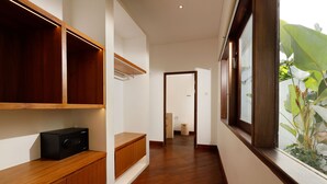 A hallway with wooden flooring, built-in shelves, and a window with a view of greenery. - Villa Perere9 by Nakula (Canggu)