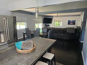 A modern kitchen with a dining area, a built-in TV, and a large window. - Spacious home near Torch Lake w/custom back patio, steps away from public access (Alden)