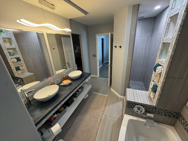 A modern bathroom with dual sinks, a large mirror, and a walk-in shower.