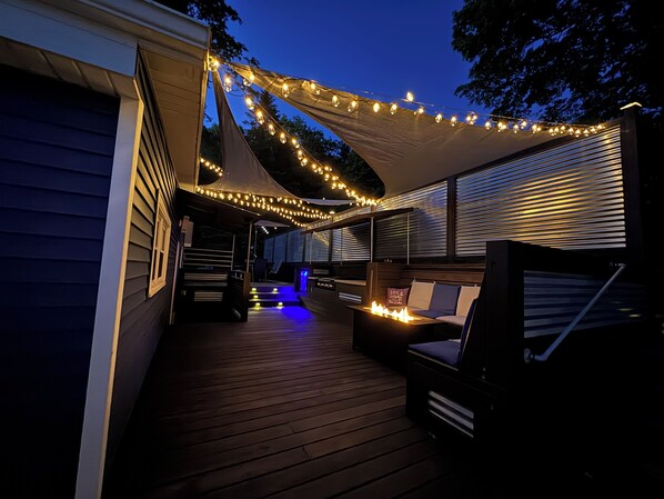 A covered outdoor deck with string lights, a bench, and a fire feature.