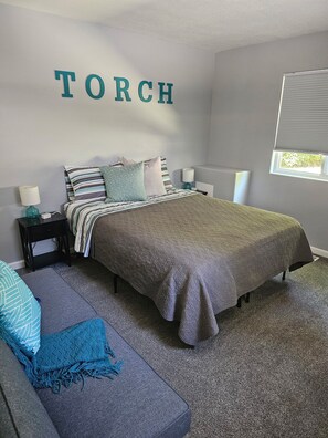 A bedroom with a bed, two nightstands, a bedside table, a window, and a wall-mounted sign.