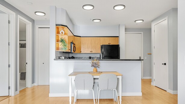 A modern kitchen with wooden cabinets, a black refrigerator, and a white countertop. - River Downtown Condo, A/C, Underground Parking, Saddledome & Stampede (Calgary)