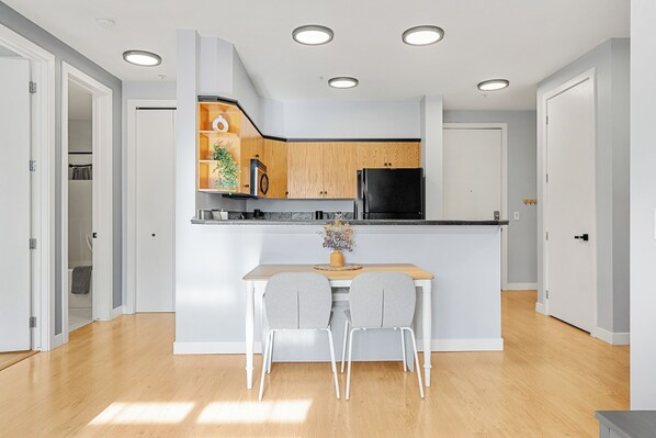 Une cuisine moderne avec des meubles en bois, un réfrigérateur noir et un plan de travail blanc.